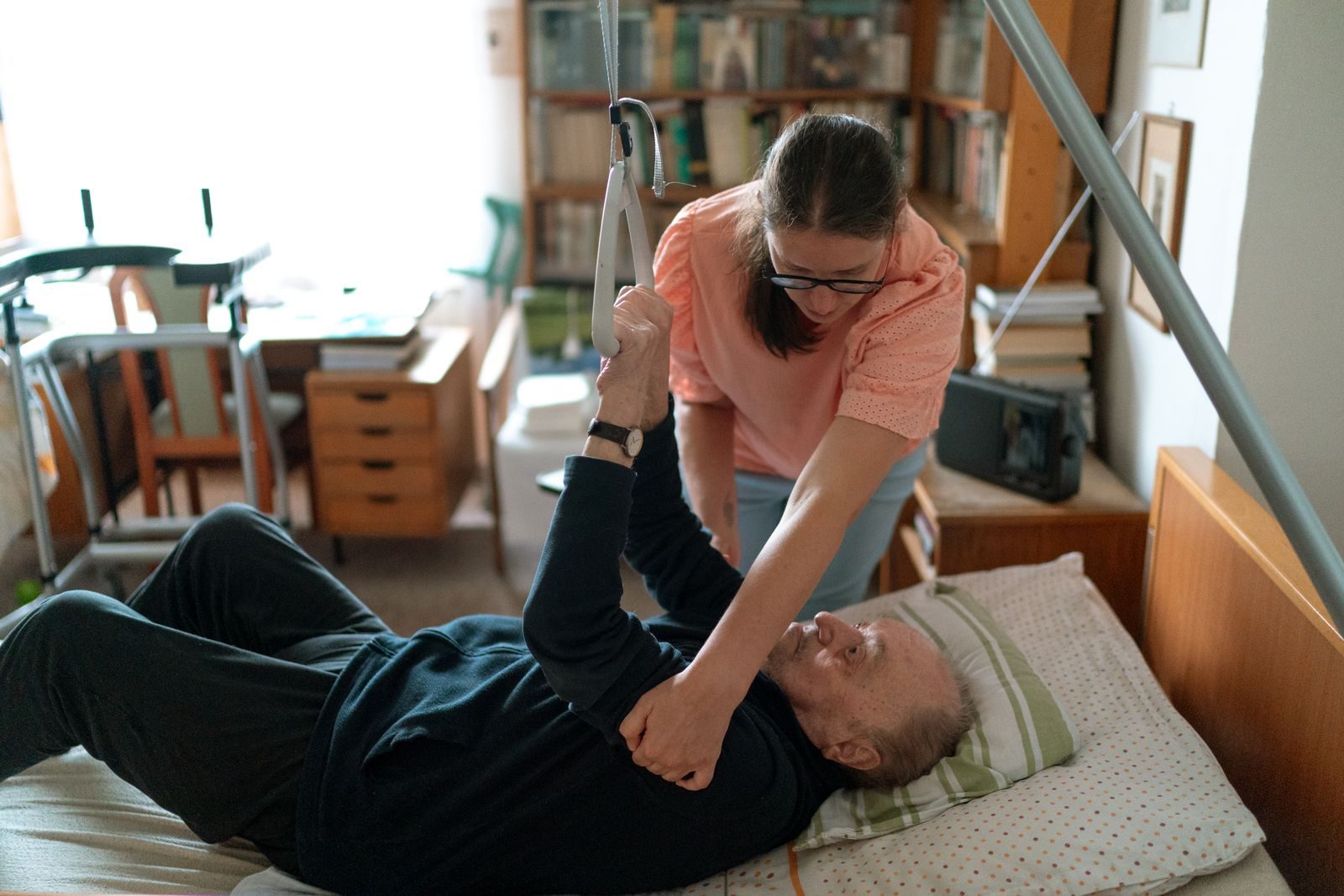 Physiotherapist assisting an older patient with exercises on a bed at home